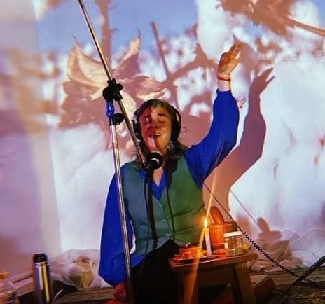 Viky cantando frente al micrófono, con las proyecciones del paisaje detrás